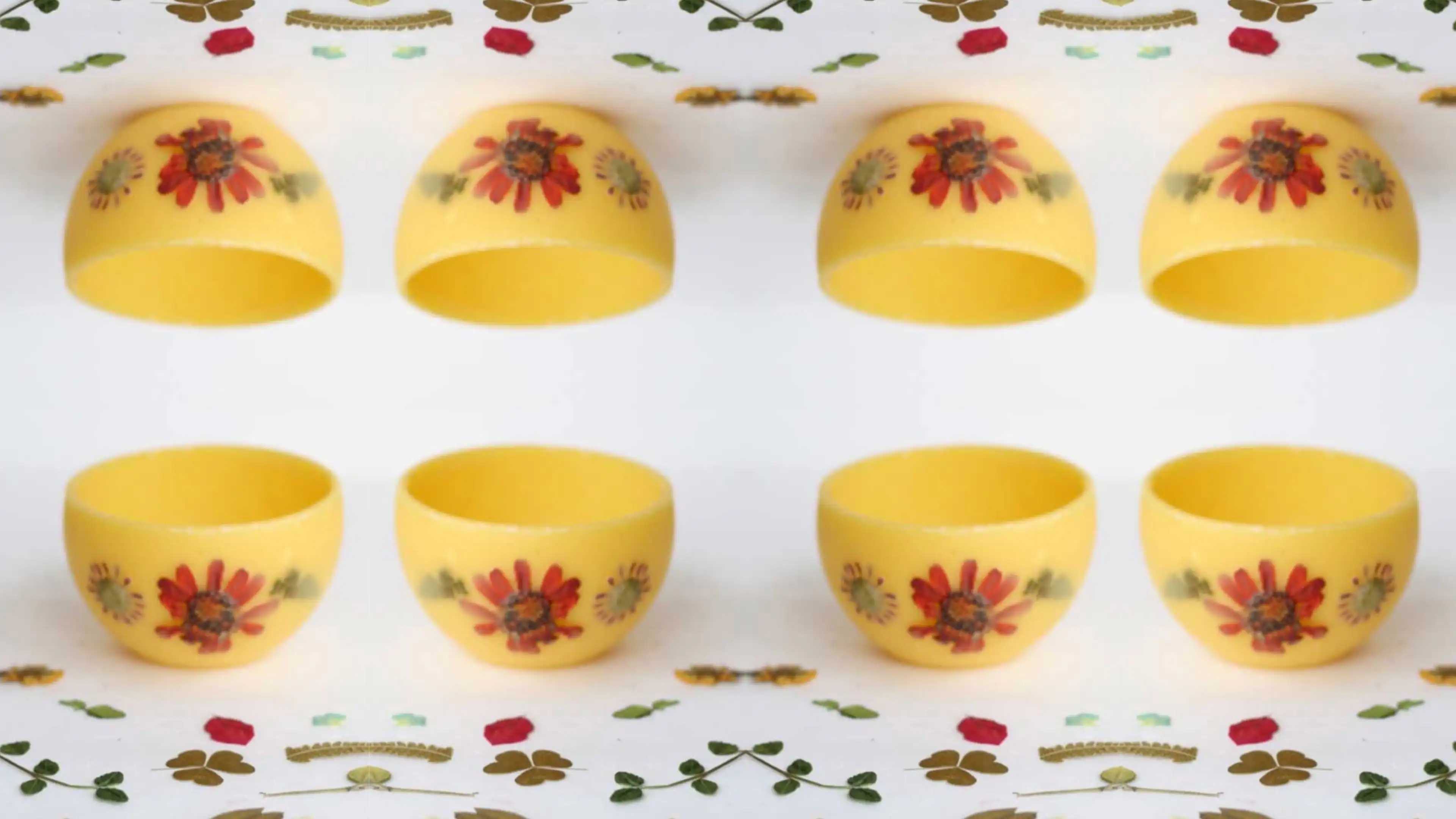 Yellow handcrafted bowl and matching domes decorated with red flowers, repeated in a pattern.